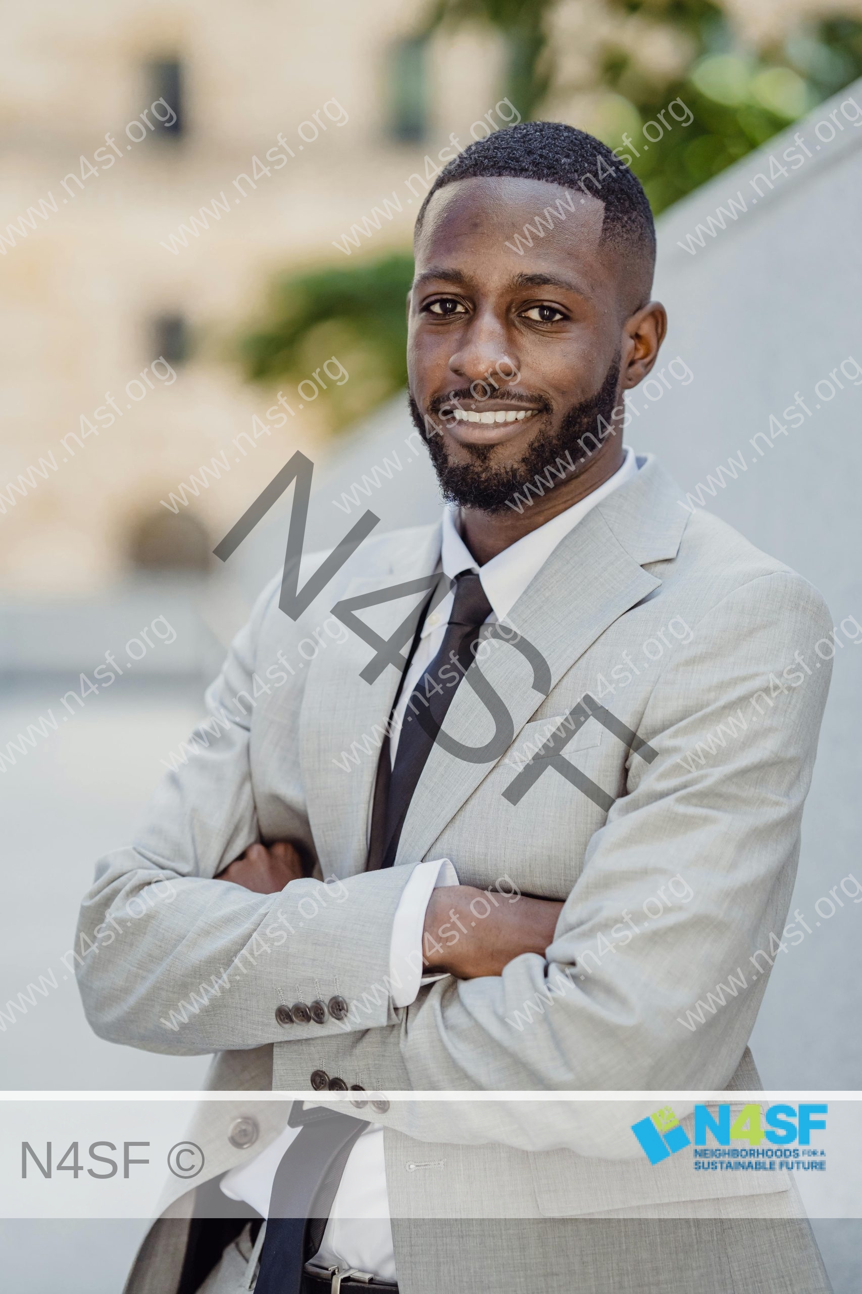 A confident businessman in a gray suit, smiling and posing outdoors with arms crossed.